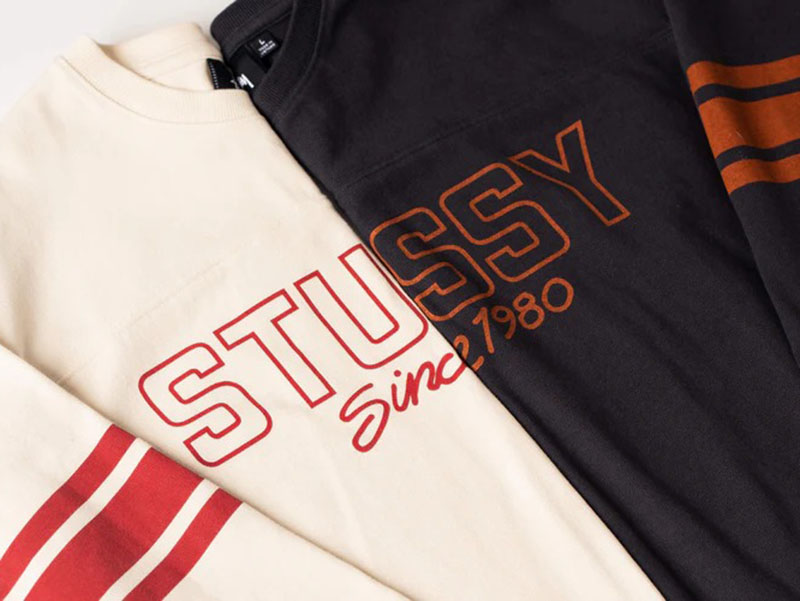 Cream and black graphic sweatshirts with bold varsity-style logo prints and striped sleeves