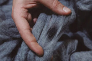 Hand holding soft gray acrylic fiber strands, highlighting lightweight texture, warmth, durability, and synthetic textile material used in knitwear production.
