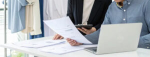 Fashion industry professionals reviewing apparel documents and laptop during clothing business planning and production management meeting