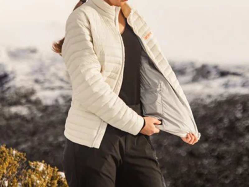 Person wearing cream-colored lightweight outdoor jacket in snowy landscape