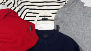Flat lay of red, gray, navy, and striped cashmere sweaters neatly arranged on a white background.