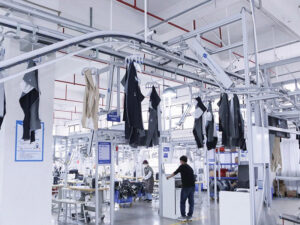 Modern garment manufacturing facility with automated conveyor system transporting clothing pieces through production line.