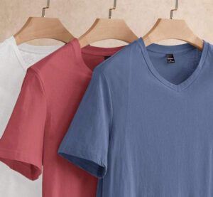 Three V-neck t-shirts in white, pink, and blue hanging on wooden hangers.