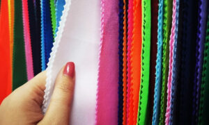Hand holding bright multicolored polyester fabric swatches with pinking sheared edges.