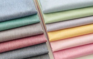 Neatly folded fabric in various pastel shades arranged side by side, showing smooth texture and soft colors