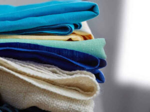 Hands holding a variety of fabric swatches in different colors and textures for clothing selection.
