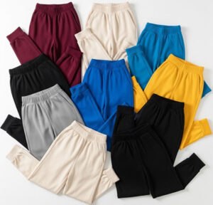 Stack of colorful sweatpants in black, blue, yellow, grey, burgundy, and cream laid out neatly on a flat surface