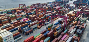 Aerial view of a busy container port with stacked shipping containers, cargo cranes, and logistics infrastructure supporting global trade and international freight transportation.