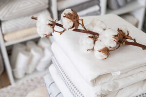 Cotton branch resting on neatly folded white fabrics, highlighting natural cotton material, softness, breathability, and sustainable home textile production.