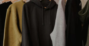 Assorted cotton hoodies in black, grey, and olive hanging on wooden hangers.