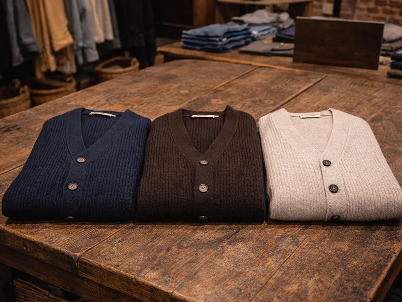 Three folded ribbed cardigans in navy, brown, and light gray.