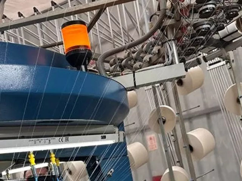 Industrial textile knitting machine processing yarn spools in a modern factory, showcasing automated fabric production and advanced garment manufacturing technology.
