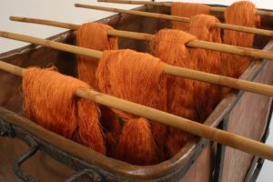 Orange yarn being dried on wooden rods in a dye bath for textile production.