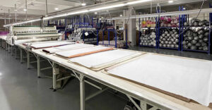 Rolls of various fabrics laid out on a large cutting table in textile factory.