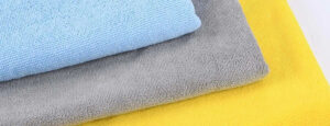 Stacked fleece fabric samples in blue, gray, and yellow, highlighting soft texture, warmth, and insulating material properties for apparel and outerwear.