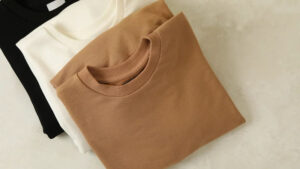 Stack of folded crew neck T-shirts in black, white, and beige colors, showcasing soft fabric, casual style, and everyday wardrobe essentials.