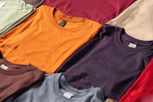 Multiple folded T-shirts in various colors laid out on a surface.