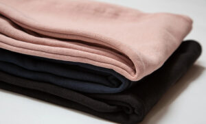 Stack of three neatly folded cotton knit fabrics in pink, navy, and black on a white surface.