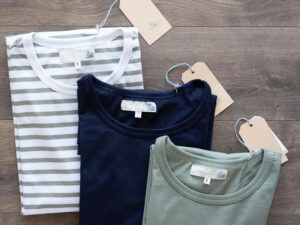 Three folded T-shirts in striped, navy, and green colors with attached price tags on wooden surface.
