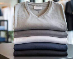 Stack of neatly folded V-neck T-shirts in gray, white, navy, and black colors on a store display or table