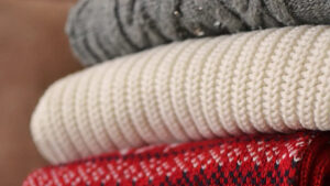 Close-up of stacked folded winter sweaters in grey, white, and red knit textures.