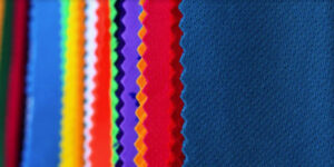 Colorful performance fabric swatches with textured mesh surfaces, showcasing breathable materials used for football uniforms and athletic sportswear manufacturing.