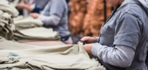 Workers inspecting and folding garments on production line inside busy clothing manufacturing factory environment