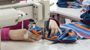 Worker operating an industrial sewing machine to stitch colorful fabric panels, demonstrating garment manufacturing, apparel production, and textile craftsmanship in a clothing factory.