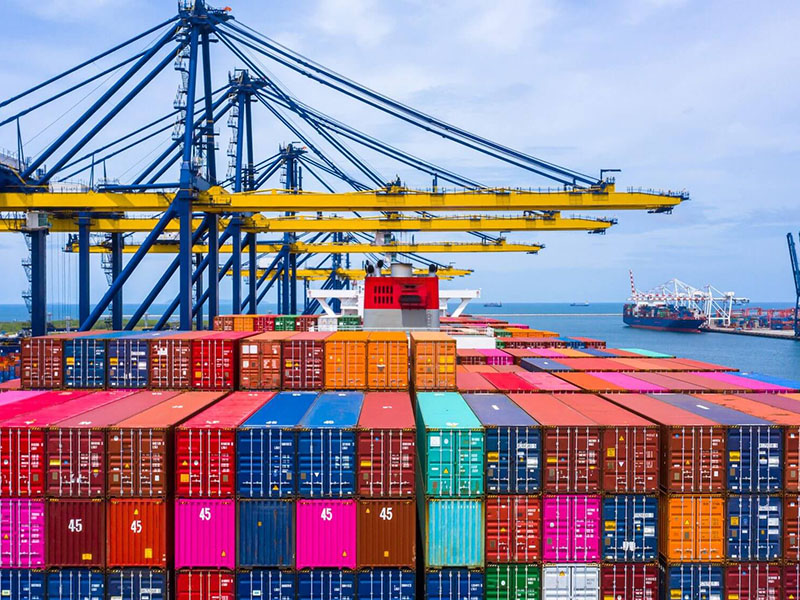 Large container shipping port with stacked colorful cargo containers and cranes loading vessels.