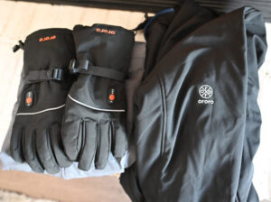 Black Ororo heated gloves with adjustable straps and matching heated jacket on display.