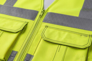 Close-up of high-visibility safety vest featuring reflective tape, durable zipper closure, and reinforced utility pockets for workplace protection.