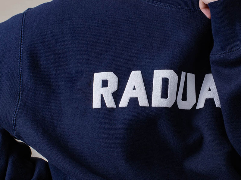 Close-up of navy hoodies featuring raised puff print lettering, showcasing premium screen printing texture and custom apparel branding details.