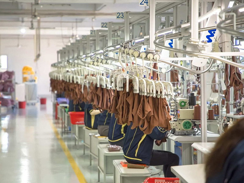 Workers sewing brown activewear garments on assembly line machines.