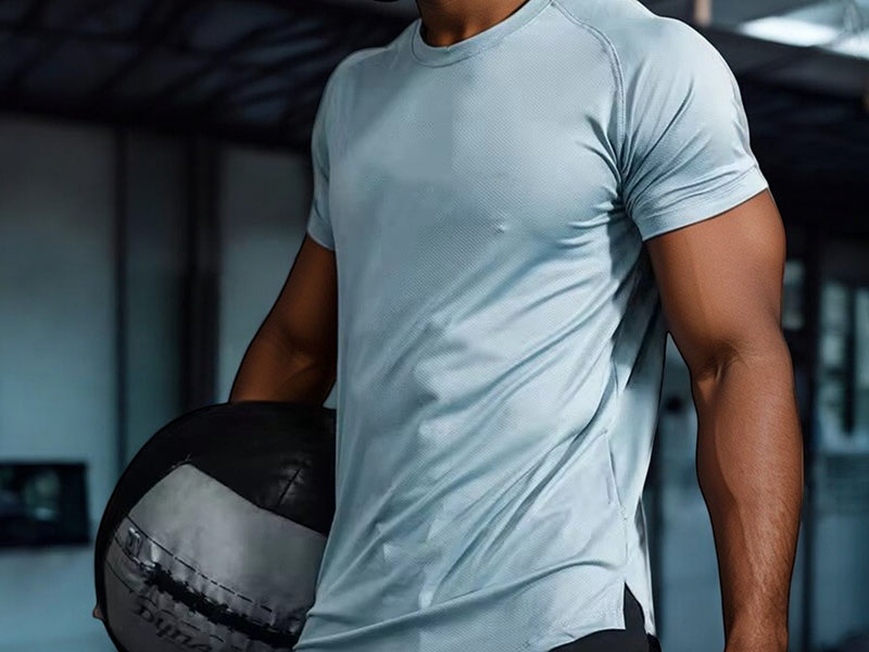 Close-up of a man wearing a fitted light gray athletic t-shirt holding a medicine ball, highlighting the breathable performance fabric.