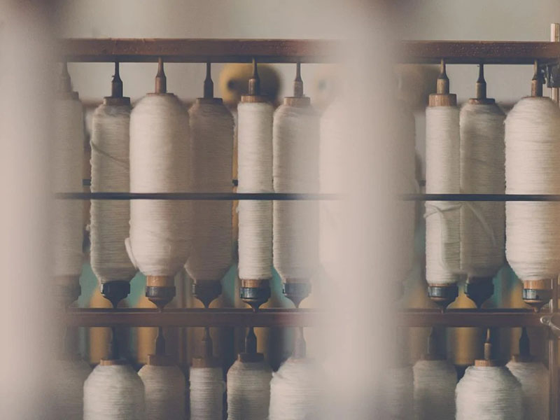 Textile yarn spools arranged on industrial racks, showcasing raw cotton and polyester fibers used in polo shirt fabric manufacturing.