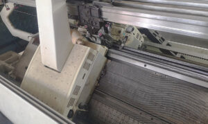 Industrial knitting machine producing textile with needles and threads in motion.