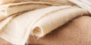 Close-up of soft folded cashmere fabric in cream and beige tones, highlighting fine knit texture, lightweight warmth, and premium luxury apparel material.
