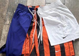 Pair of blue, white, and orange Nike basketball shorts laid flat on wooden floor.