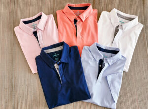 Five folded men’s polo shirts in pastel and classic solid colors displayed neatly on textured background for casual fashion collection