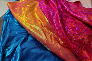Colorful metallic spandex fabrics in blue, gold, and pink with shiny reflective textured surfaces.