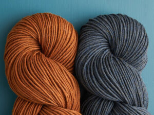 Two skeins of yarn, one orange and one blue, neatly twisted against a teal background.
