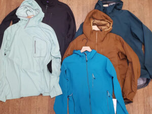 Five assorted outdoor jackets in different colors and styles laid out on a wooden floor.