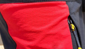 Close-up of red perforated performance fabric panel with breathable micro-ventilation holes and reinforced black trim, designed for activewear, outdoor apparel, and durability.