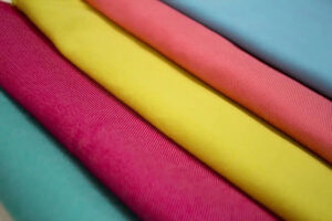 Colorful polyester spandex fabric rolls in pink, yellow, coral, and blue, showcasing smooth texture, stretchability, and vibrant activewear material options.