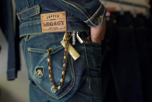Close-up of premium raw denim jeans featuring leather brand patch, contrast stitching, back pocket details, and classic selvedge denim craftsmanship.