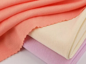 Three pieces of soft rayon jersey fabric in coral, cream, and lavender, folded and layered on a white surface.