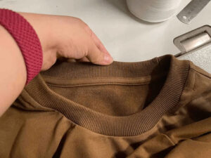 Close-up of brown sweatshirt crew neck with ribbed collar and soft fleece lining, highlighting garment construction, stitching details, and premium fabric quality.