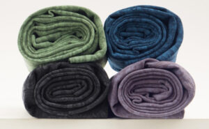 Four rolled knit fabric pieces in green, blue, black, and purple shades stacked neatly for textile and apparel production.