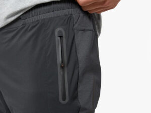 Close-up of dark gray men’s jogger pants with elastic waistband and drawstring, worn with sneakers.
