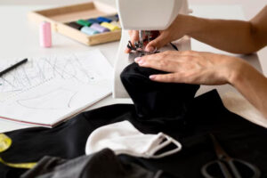 Close-up of hands sewing black fabric on a machine in a clothing workshop.